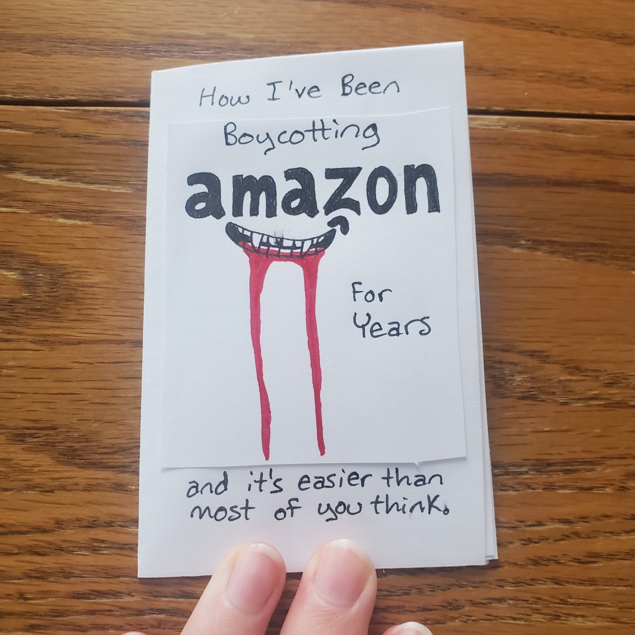 ID: Photos of a mini zine on a wood table. The title is How I've Been Boycotting Amazon For Years and it's easier than most of you think. The amazon logo smirk has been drawn as a toothy, bloody mouth. The next page includes several news headlines about amazon removing DEI, labor violations, and deaths of employees. The next page includes tips for reading. Number one is don't allow defensiveness to get in the way of making change. Number two says before you tell me there is no ethical consumption under capitalism, ask yourself am I using this phrase to avoid examining my own behavior. Number three says many people think they can't until they actually try. The next page says instead of amazon dot com, I use ebay, stores' actual websites, small artists, and secondhand shopping apps. The next photo shows two pages on reading, groceries, and media. For reading, storygraph. For groceries, pretty much anything other than whole foods. For media, don't use twitch or audible. Instead, use youtube, libby, hoopla, antennapod, or rss radio. The final photo shows the last page which says, "I realize this can be harder for some folks than others. I just hope this zine will make people consider and hopefully change their habits." CharlieTtea.
